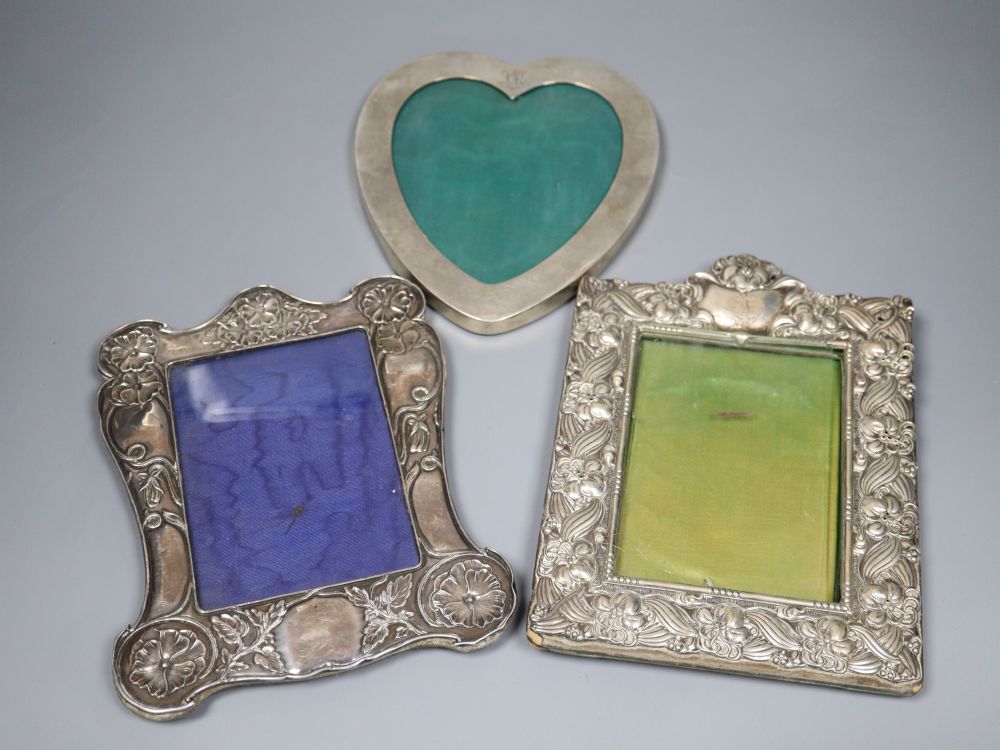 Two early 20th century repousse silver mounted photograph frames(a.f.) and a sterling heart shaped photograph frame, largest 22.5cm.